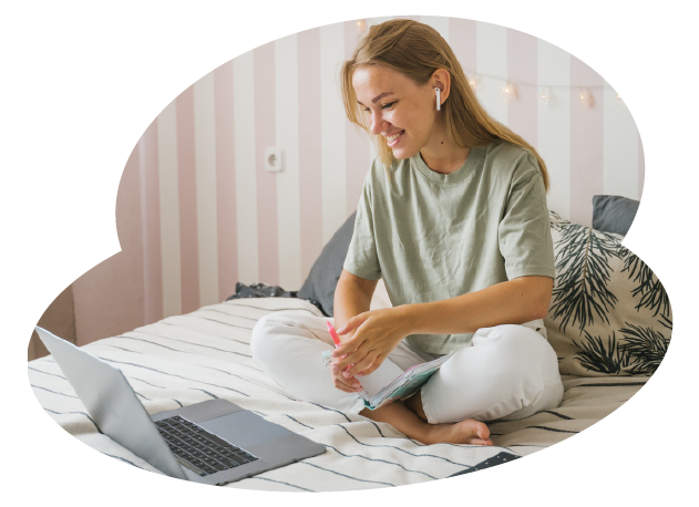 A person sat crossed-legged on a bed with a laptop in front of them where they are learning from free online courses through home learning