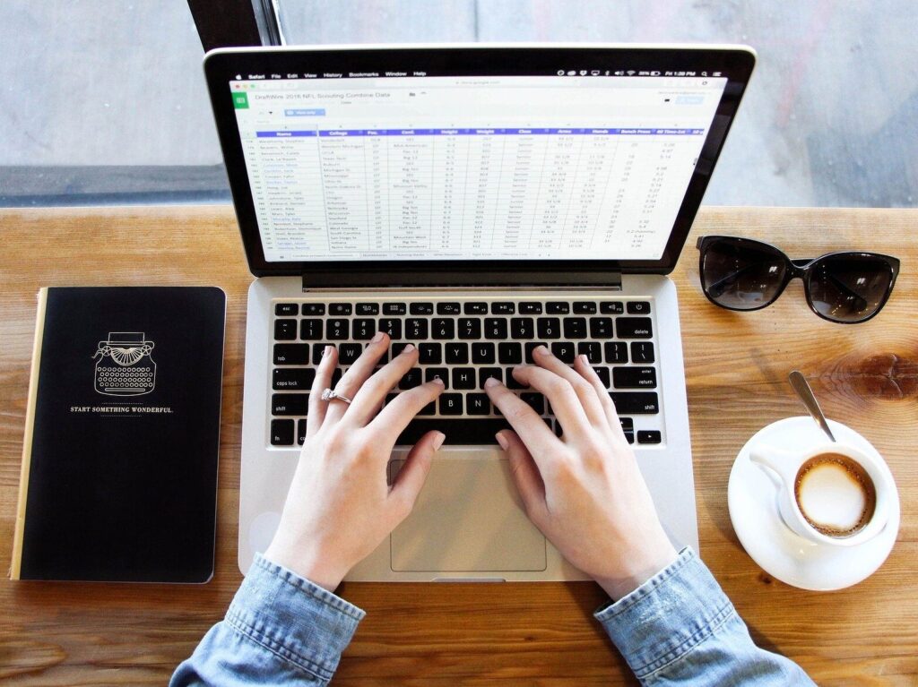 Hands typing on a laptop which shows an Excel spreadsheet
