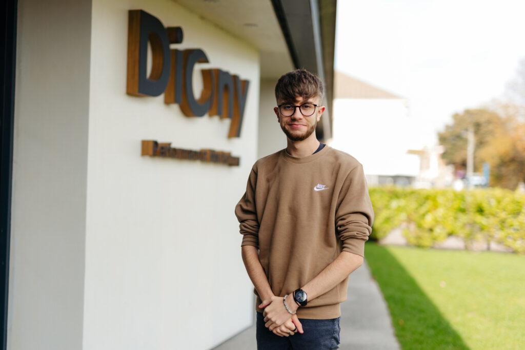 Photo of Apprentice of the Year, Sam standing in front of his Diony displaying their logo.