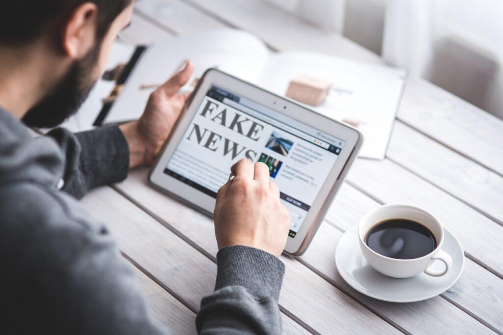 Man looking at digital tablet which shows the words "fake news" on the screen