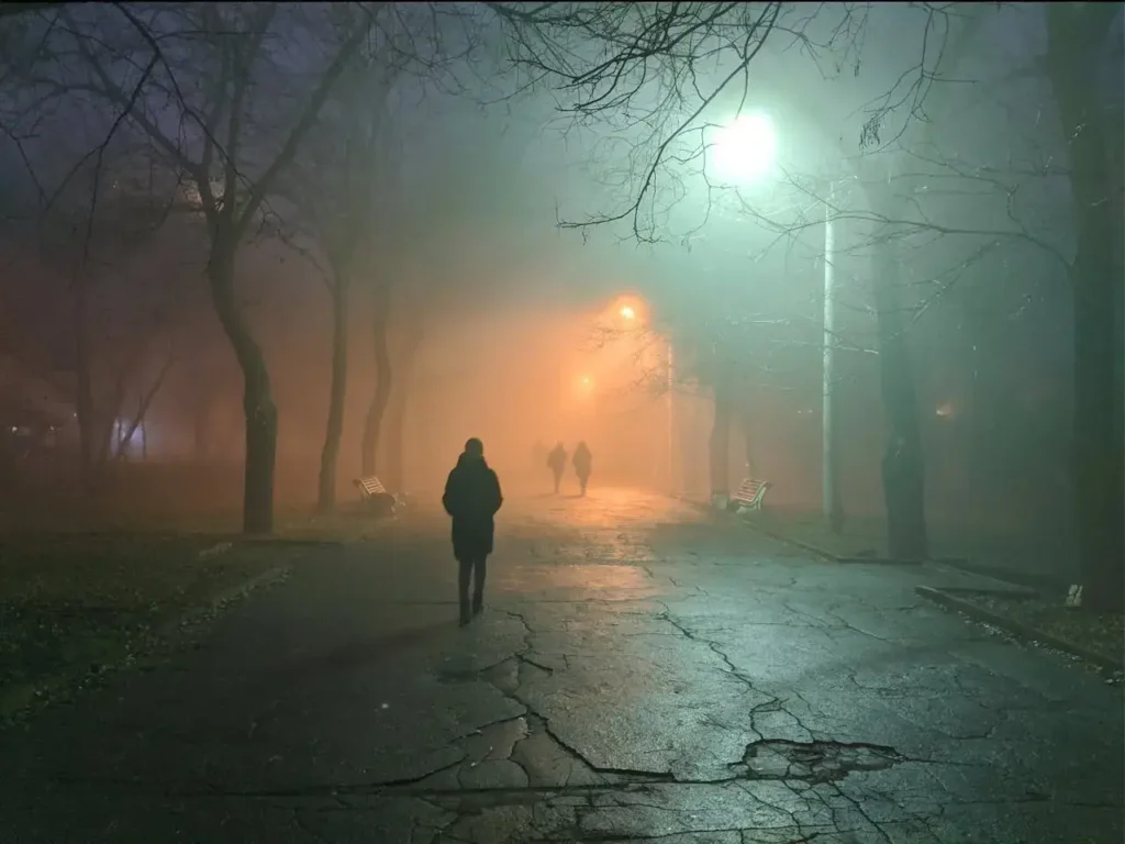 Photo of a lone person walking through a streetlight park. Staying safe in the dark.
